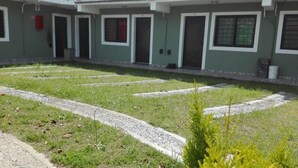 Un edificio con varias puertas y ventanas, un camino de grava y algo de vegetación en primer plano.