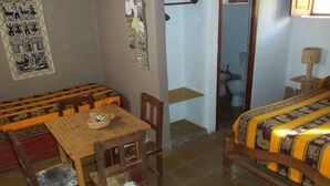 Une pièce comprenant une table et des chaises en bois, un lit recouvert d’une couvre-lit à motifs et un mur orné d’un panneau décoratif.