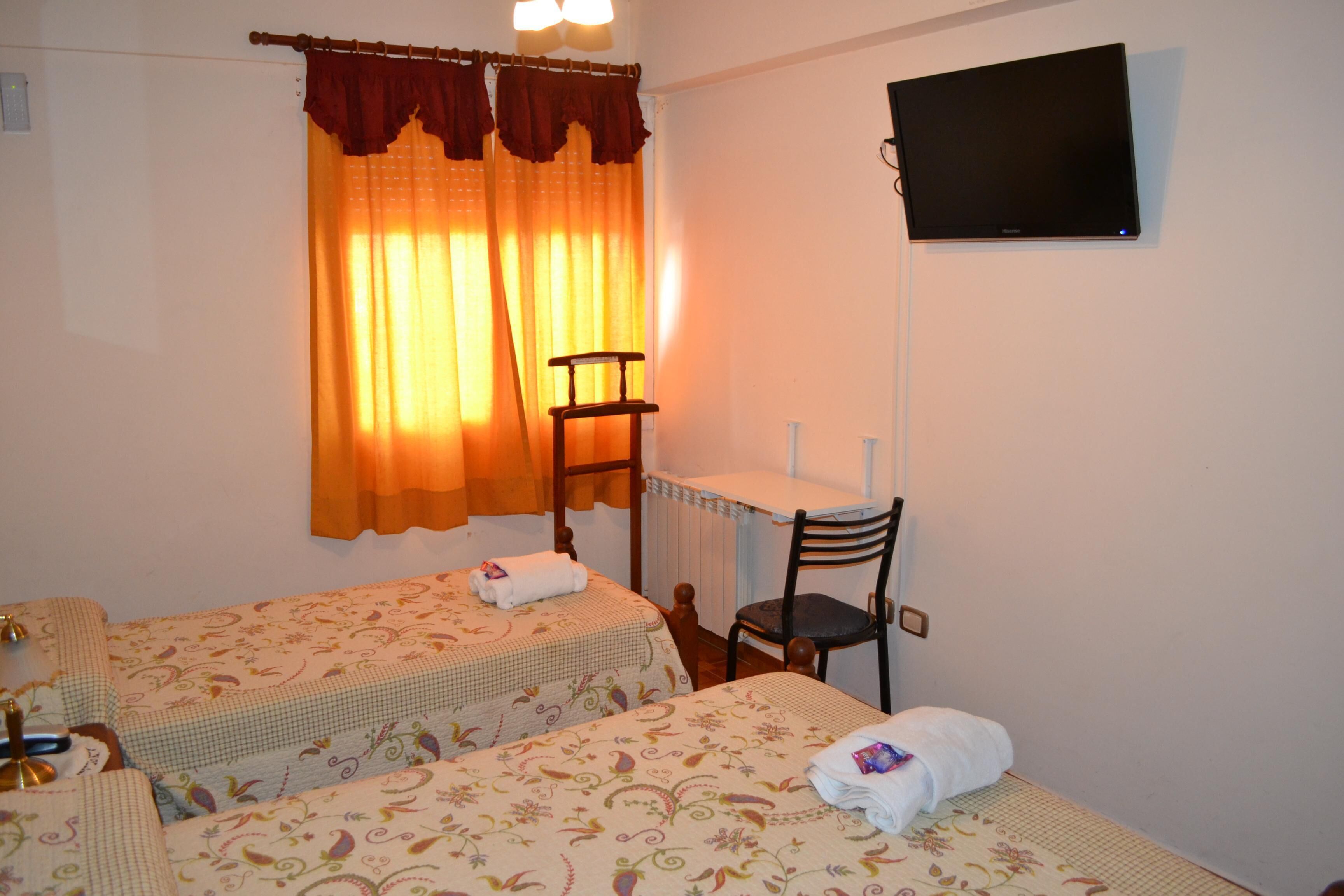 A hotel room with two beds, a desk, a chair, and a TV.
