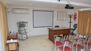 Een vergaderruimte met een groot scherm, een houten bureau, meerdere stoelen en een airconditioner.