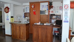 Een receptiezone met houten balies, een ventilator, een computer en diverse informatieposters.
