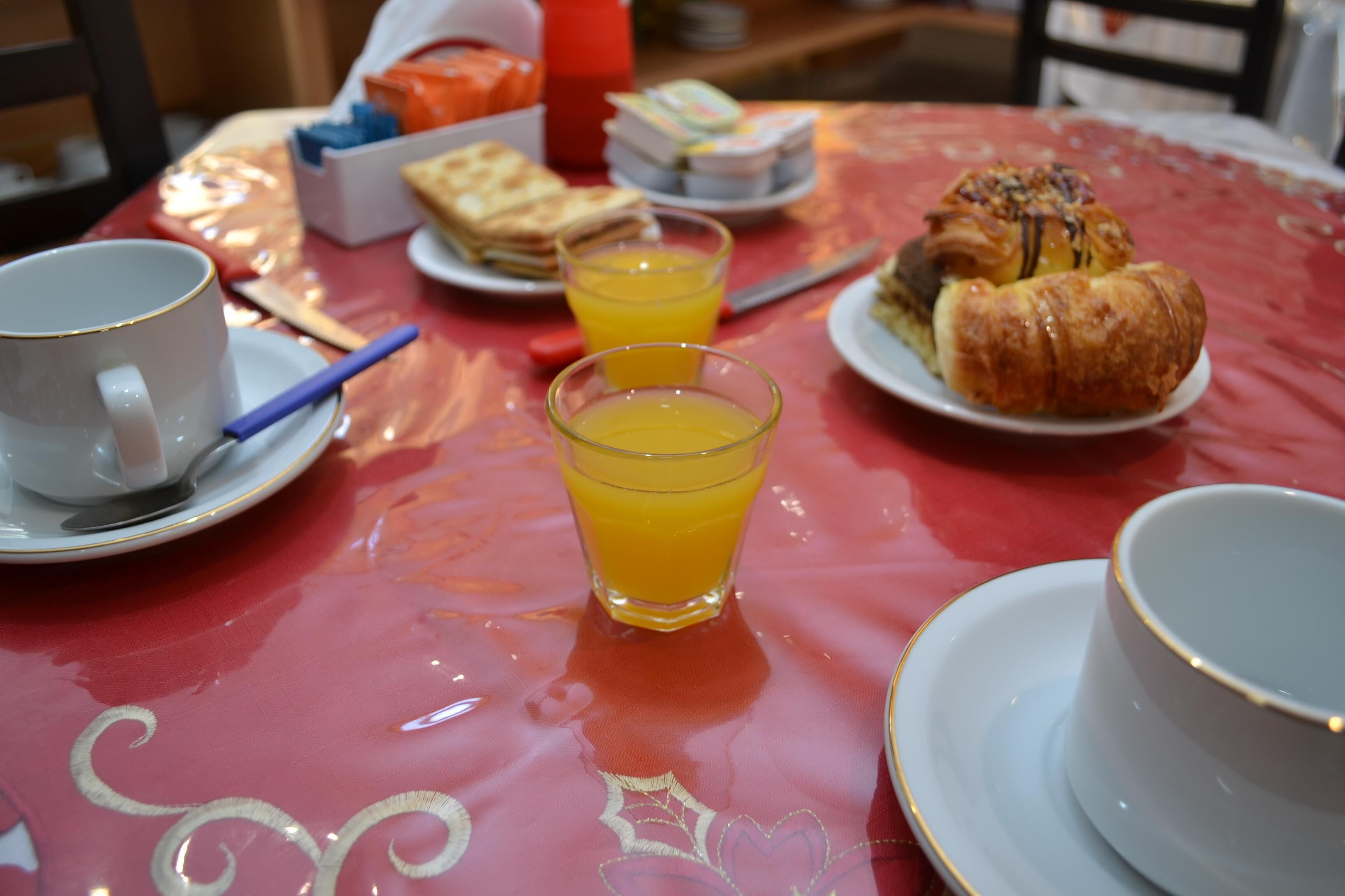 A breakfast table with a cup, a glass of orange juice, a croissant, and a plate of sandwiches.