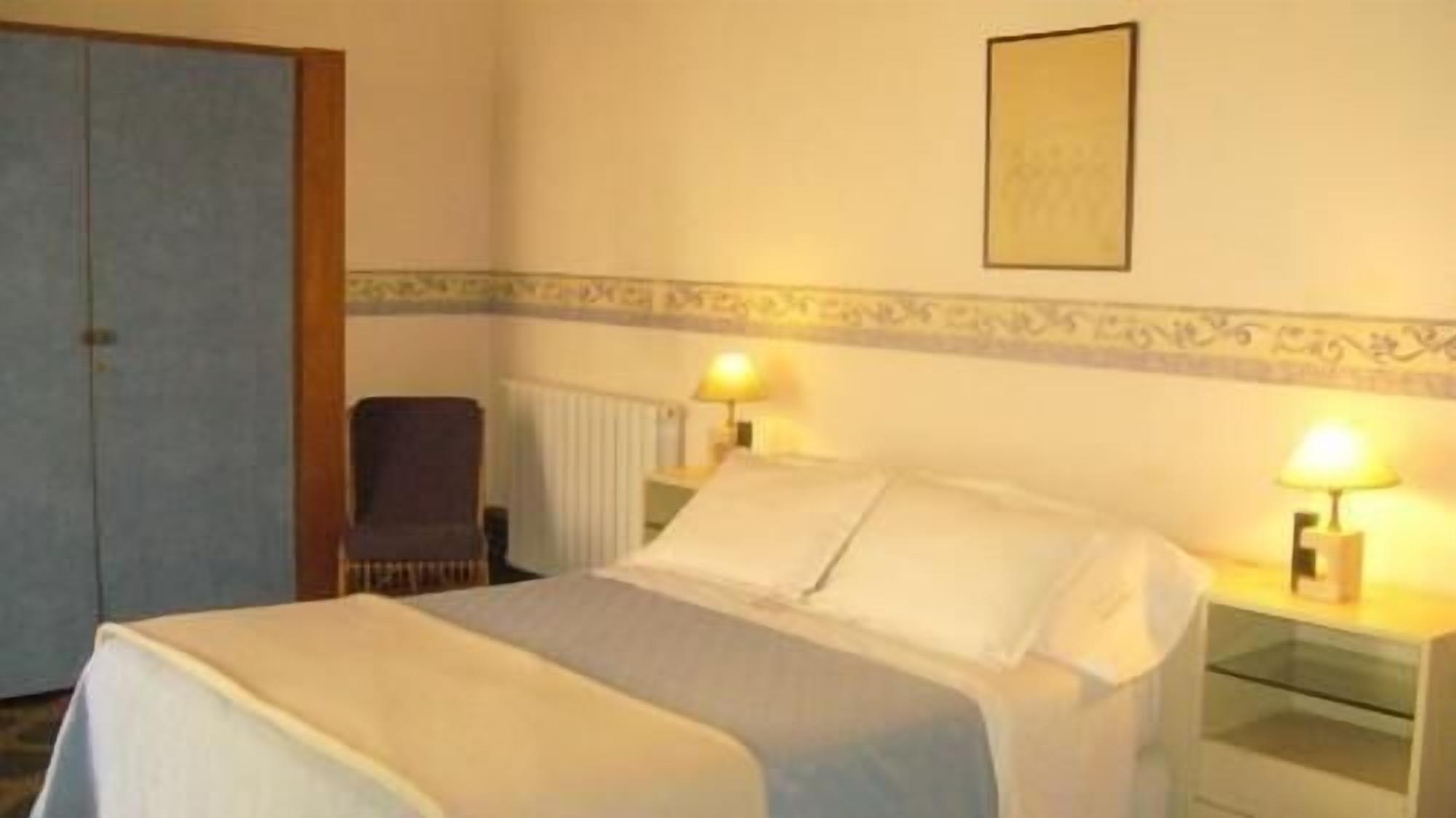 A hotel room with a bed, two bedside lamps, a chair, and a door.