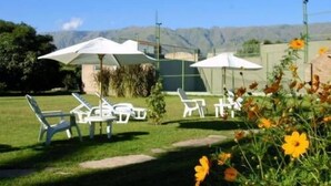 Un'area patio con poltrone da lounge bianche e ombrelloni, un tavolino e vista sulle montagne sullo sfondo.