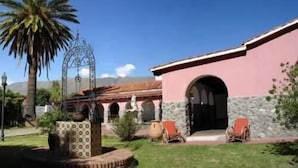 Un edificio con facciata rosa, dettagli in pietra e un patio con sedie e una palma.