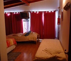 Una habitación pequeña y acogedora con dos camas, un televisor montado en la pared y cortinas rojas.