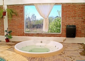 Habitación de spa con ventana grande, pared de ladrillo, bañera y un altavoz.