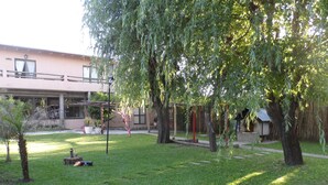 A grassy courtyard with trees, a small fountain, and a building in the background. - La Casona (Gualeguaychú)