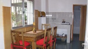A dining area with a wooden table and chairs, a window with bars, and a kitchen in the background. - La Casona (Gualeguaychú)