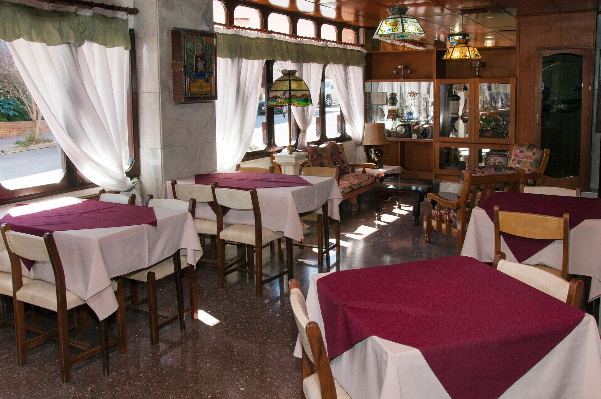 A restaurant interior with tables set for dining, chairs, and a display of various items on shelves.