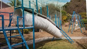 A playground with a large spiral slide, blue metal structures, and a swing set. - Gran Hotel Tomaso Di Savoia (La Falda)