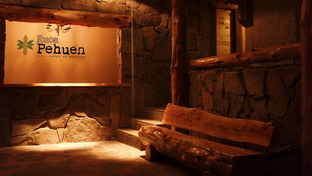 A rustic interior with a stone wall, wooden bench, and a sign reading "Ruca Pehuén ECO - LODGE DE MONTAÑA". - Ruca Pehuen Eco Lodge de Montaña (Caviahue)
