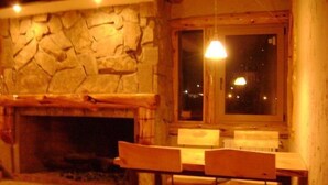 A stone fireplace with a rustic wooden table and chairs. - Ruca Pehuen Eco Lodge de Montaña (Caviahue)