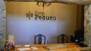 A reception desk with a wooden top, a sign reading "Ruca Pehuén ECO - LODGE DE MONTANA", and a stone wall. - Ruca Pehuen Eco Lodge de Montaña (Caviahue)
