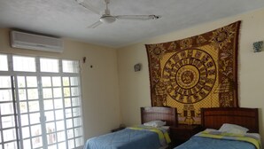A room with two beds, a ceiling fan, and a large tapestry on the wall. - Paakal's Hostel (Chetumal)