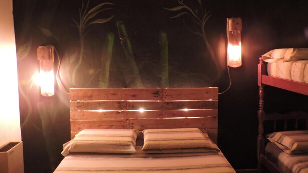 Un letto in legno con testiera, due lampade sui comodini e un muro decorato con un murale di piante.