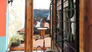 Un balcone in legno con una bicicletta, piante in vaso e un murale sulla parete.