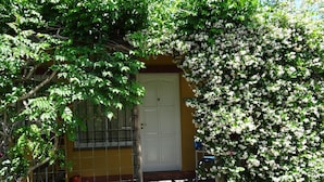 Un bâtiment jaune avec une porte blanche, entouré d’une végétation luxuriante et d’un mur couvert de lierre.