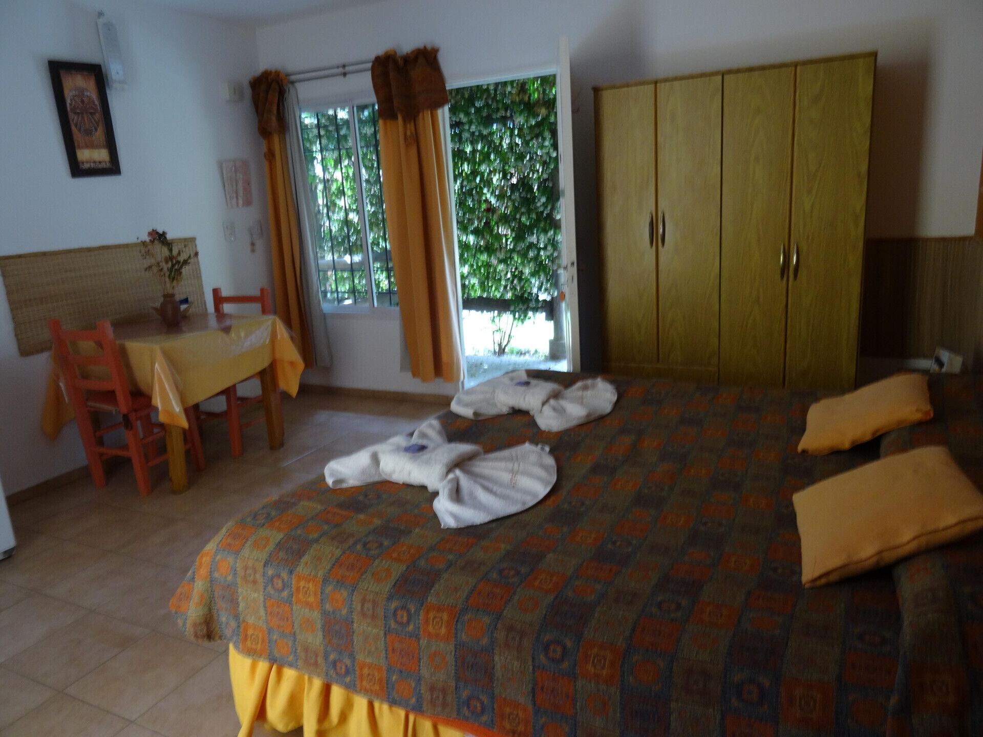 Ein Schlafzimmer mit einem Bett, einem Holzschrank, einem Tisch mit Stühlen und einem Fenster mit Vorhängen.