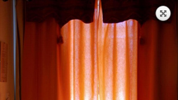 Une table avec une bouteille de vin et deux verres, un set de table rouge et un menu, dans une pièce à l’éclairage chaleureux, décorée de rideaux orange.