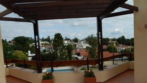 Un balcon fermé offrant une vue sur un quartier résidentiel, avec une piscine et des plantes en pot.