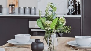 A modern kitchen with a wooden table set for dining, a vase with greenery, and a black decorative object. - Stylish new-build FREE parking, 10min to BHX & NEC (Birmingham)