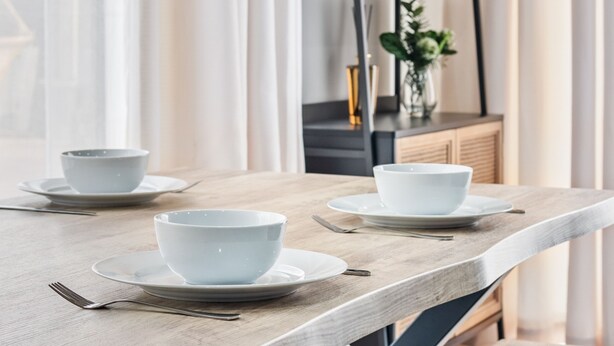 A dining table with two white bowls and plates, a fork, and a knife. There is a black metal shelf with glassware in the background. - Stylish new-build FREE parking, 10min to BHX & NEC (Birmingham)
