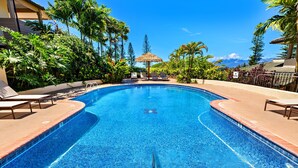 Ein Swimmingpool mit klarem, blauem Wasser, umgeben von Palmen und Liegestühlen.