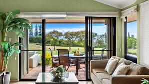 Ein Wohnzimmer mit einer Couch, einem Couchtisch und Blick auf einen Golfplatz durch große Schiebeglastüren.