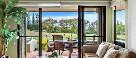 A living room with a sofa, a coffee table, and a view of a golf course through large sliding glass doors.