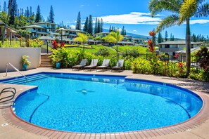 A circular pool with lounge chairs, surrounded by a landscaped garden and a view of residential buildings.