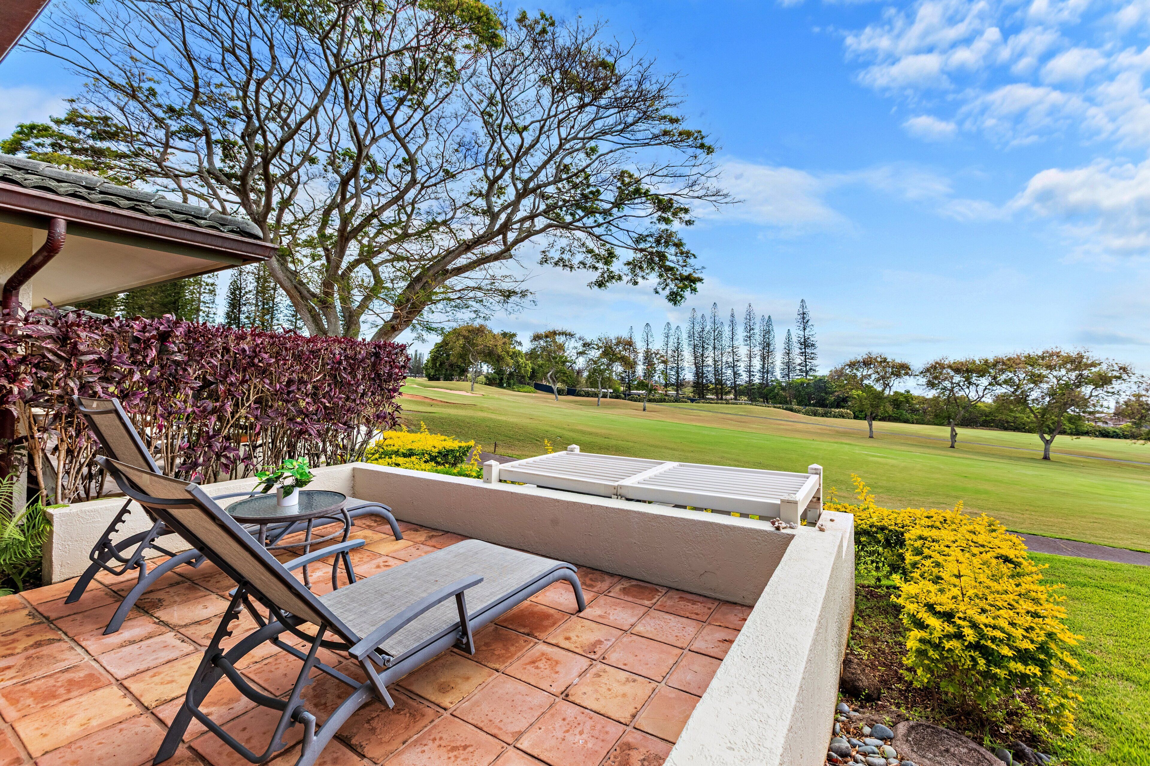 A patio with two lounge chairs and a small table, overlooking a well-maintained lawn and trees.
