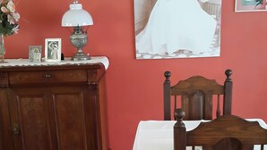 Een eethoek met een houten tafel en stoelen, een kast met decoratieve objecten, en een wand met ingelijste foto's en een groot schilderij.