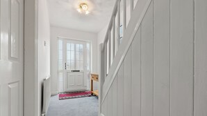 A hallway with a white door, a small wooden table, and a red rug on a grey carpet.