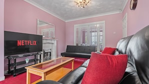 A living room with a black leather sofa, a wooden coffee table, a flat-screen TV, and a red carpet.