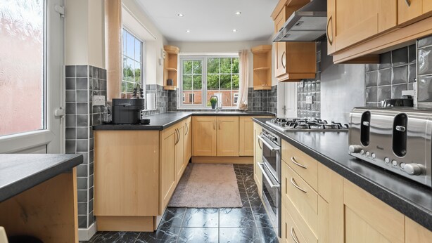 A modern kitchen with wooden cabinets, black countertops, and a large window providing natural light.