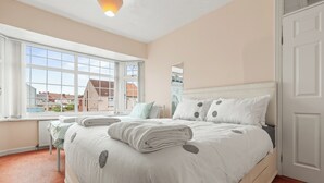 A bedroom with a large bed, a window with a view of buildings, and a door.