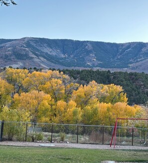 Un pati tancat amb zona de jocs, gespa i un fons d’arbres de colors tardanes i muntanyes llunyanes.