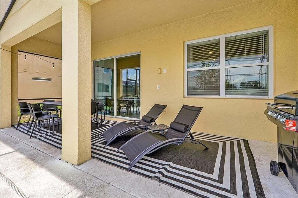 Un patio exterior con sillones de descanso, una parrilla y una zona de estar cubierta con mesas y sillas.