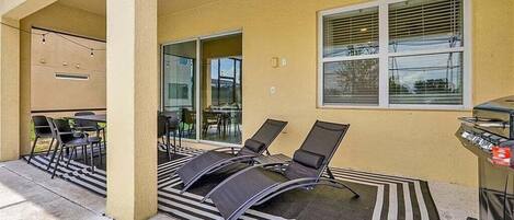 Un patio exterior con sillones de descanso, una parrilla y una zona de estar cubierta con mesas y sillas.