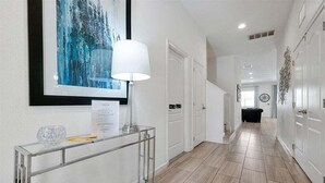 A hallway with a glass console table, a framed artwork, and a white door. - 12BR Solterra Mansion + Arcade Game Room & Pool (Davenport)