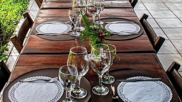 An outdoor dining area with a long wooden table set for a meal, surrounded by chairs and a speaker. - Senador Dupont (Tigre)