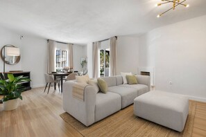 Ein modernes Wohnzimmer mit grauem Sofa, einem Esstisch und einem großen Fenster.