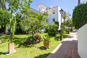 Ein gepflegter Garten mit verschiedenen Pflanzen und einem Weg zu einem weißen Gebäude mit Ziegeldach.
