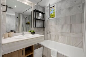 Ein modernes Badezimmer mit einem großen Spiegel, einem Waschbecken, einer Badewanne und einem Fenster mit Blick auf Bäume.