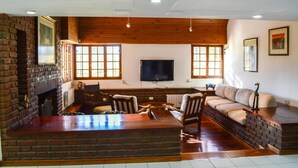 A living room with a brick fireplace, wooden ceiling, a television, and a sofa. - Casa Bonita (Neuquén)