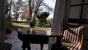 A room with a view of trees and a patio. There is a table and a chair with a striped cushion. - Casa Bonita (Neuquén)