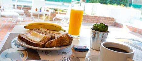 Una escena de desayuno con tostadas, un plátano, un vaso de jugo de naranja, una taza de café y una planta pequeña sobre una mesa.