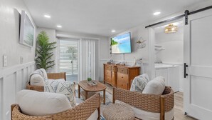 A living room with wicker furniture, a television, and a sliding door leading to a kitchen. - 197 Beach Daze: 3BR Pool Home w/ Deeded Beach Access! (Fort Myers Beach)