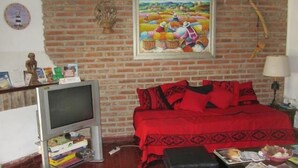 A room with a brick wall, a bed with red bedding, a television on a stand, and a painting above the bed. - Paraná Hostel (Parana)